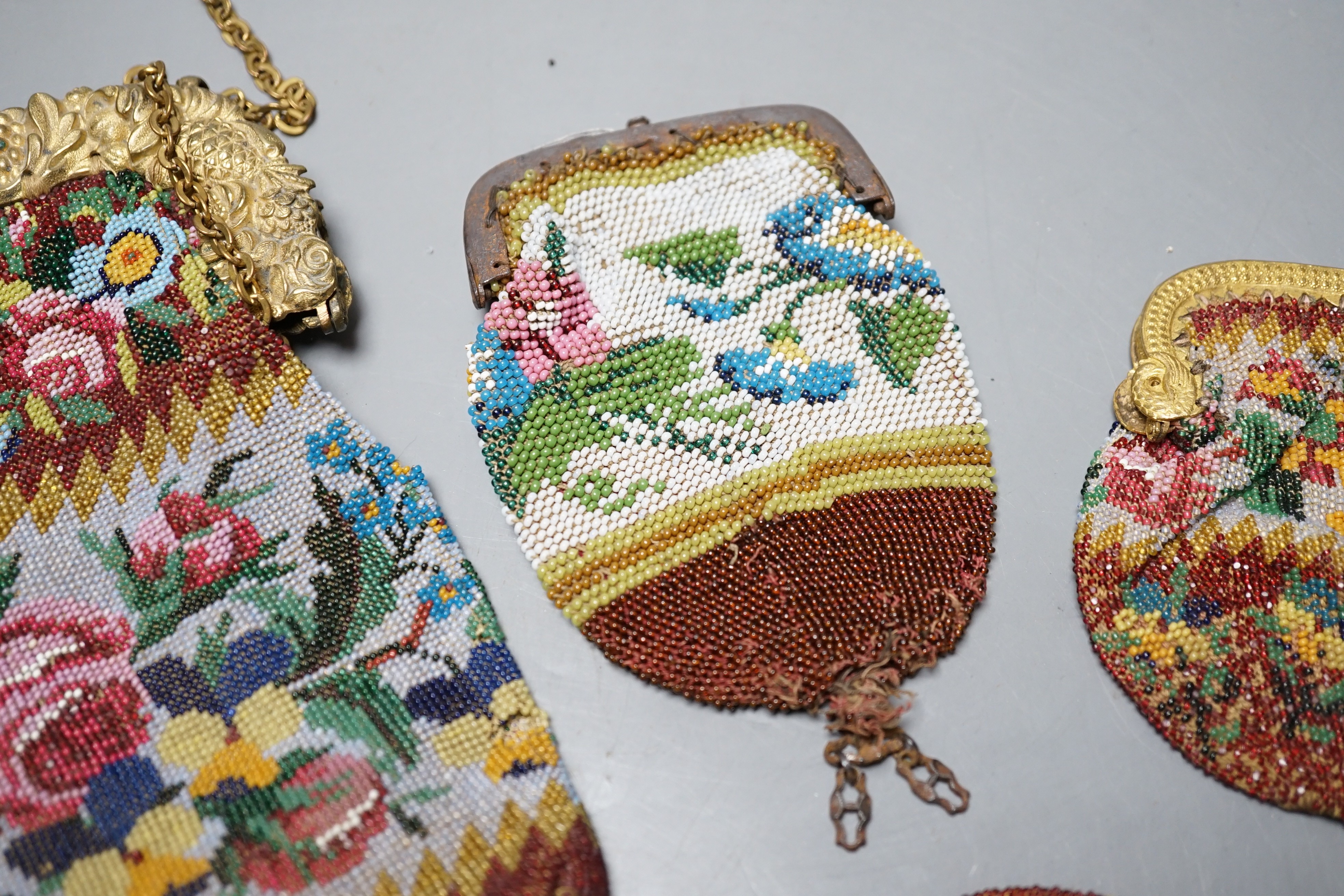 An early 19th century ornate gilt framed beaded bag with multi coloured floral design, together with three similar worked purses, gilt framed bag 20 cms high